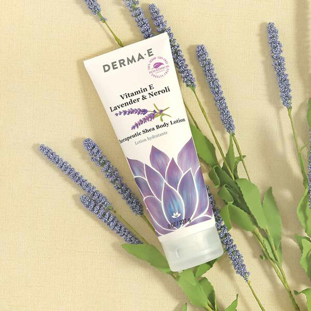 Derma E Vitamin E Shea Body Lotion tube with lavender and neroli branding, surrounded by fresh lavender sprigs on beige backg